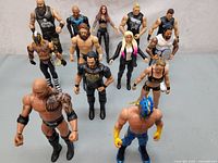 Wide shot showing all 14 WWE wrestling figures arranged in rows on a grey surface.