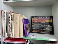 Shelf view showing eight white-jacketed hardcovers, one purple hardcover and one black softcover book