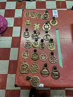 Overview of entire collection of brass horse medallions laid out on red surface showing 22 pieces in rows with some leather straps present.