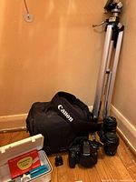 Overall shot showing camera body, carrying case, tripod, lens and accessories case on floor