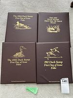 Four brown folios with gold embossed duck illustrations and titles for the years 1982, 1983, 1984, and 1986 arranged on a carpeted floor.