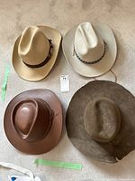 Four cowboy hats shown from above on carpet: two light beige felt Biltmore hats with braided bands, brown leather hat, and dark felt hat with damage.