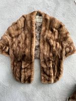 Full front view of a light brown mink fur stole laid flat, showing the fur texture and overall shape.
