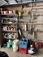 Wide view showing shelving with potted plants, garden chemicals, metal sprinklers, and plastic crates stacked underneath. Various gardening tools arranged on the wall.