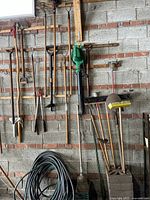 Garden tools hung on a wall including shovels, hoes, pole saw, blower, hose, and rakes.