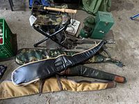 Photo showing the entire lot of hunting and camping items on a concrete floor, including rifle cases, lantern with case, folding stool, and metal pegs.
