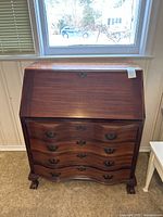 Full frontal view of the mahogany secretary desk showing four drawers and the hinged front panel closed, with carved claw feet visible.