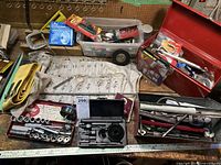 Overview of red metal toolbox on workbench with various hand tools, socket set, hole saw bits, grill stone, and miscellaneous tools and accessories.