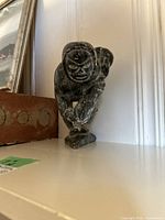 Front angled view of soap stone carving showing man holding fish, kneeling with one knee on base.