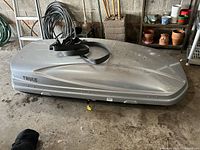 Side view of silver Thule cargo box on floor with strap draped over top.