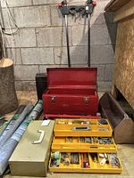 Overview showing red metal toolbox open with yellow plastic caddy holding nails, screws, and small tools visible, beige toolbox and clamps behind