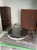 Photo showing Hitachi HT-41S turntable with clear dust cover and tonearm, three stacked Realistic Minimus speakers with brown fabric covers and wood side panels.