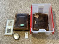 Four main items: small oval framed photo, metal double-photo frame with two photos, two old leather photo albums with one heavily damaged cover placed inside a plastic bin