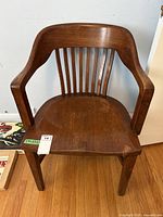 Front view of the vintage wooden desk chair showing its spindle backrest and curved armrests.