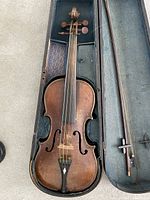 Violin inside open case showing wood finish, fingerboard, strings, bridge, and bow beside it