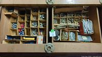 Top-down view of large wooden box with multiple compartments containing assorted bolts, nuts, washers, and electrical connectors sorted and organized.