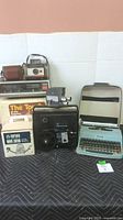 Photo showing the entire lot: Vernon movie editor, Kodak camera, Zenith clock radio, several other cameras including Polaroid and Instamatic, and Olivetti typewriter
