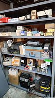 Wide view of metal shelving loaded with assorted electrical testing equipment, tool cases, chargers and supplies