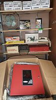 Wide view of shelving displaying various items including fan, boxed tools, phones, alarms, and fire alarm box.