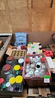 Overview of assorted jars in plastic bins and boxes, showing various sizes and lid colors including red and yellow, along with tool and drawer organizers.