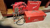 Photo showing Milwaukee heavy-duty electric hammer drill and two red metal tool boxes labeled Milwaukee Electric Hammer and Magnum.