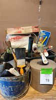 Photo showing various paint brushes, rollers, a roll of sandpaper, and paint supplies in containers.