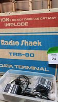 Original cardboard shipping box labeled Radio Shack TRS-80 Data Terminal, contains plastic tub with power adapters and cords