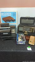 Full view of all electronics displayed together including Zenith radio, Realistic components, GE portable stereo, JVC VHS player, and cassette cabinet with box.