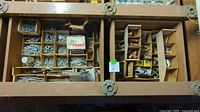Top view of large wooden box compartments containing assorted screws and various hardware items.