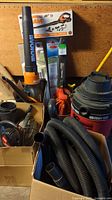Various vacuums, leaf blowers, hose extensions and accessories in boxes and loose, including a large black and orange Worx blower, visible hoses and leaf blower extension pieces.