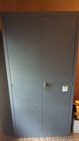 Front view of closed gray metal storage cabinet with lock, showing intact doors and metal construction.