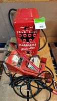 Front and slightly angled view of the red Marquette Model 32W Redi-Arc spot welder with attached cables and electrode clamp, sitting on wooden floor.
