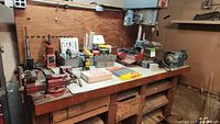Wide view showing workbench with Dayton drill press, two vises, industrial grinder, hand tools, boxes, and accessories arranged on the table.