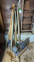 Full view of garden tools including rakes, shovels, and hand tools arranged by the wall with wheeled cart base.