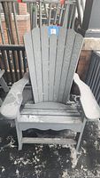 Front view of gray Adirondack chair showing slatted back, armrests, and seat covered with a layer of dirt and outdoor debris.