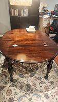 Full view of the oval antique dining table on a patterned rug with books and small objects on the table surface.