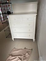 Front view of antique white painted wooden dresser with four drawers and round wooden knobs, standing on four turned legs.