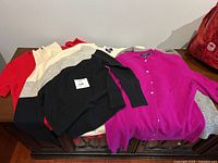 Lot of six cashmere sweaters shown together on a table in various colors including black, cream, grey, magenta, and red