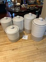 Set of five ribbed ceramic canisters in white and taupe colors with lids, arranged by size on a wooden surface