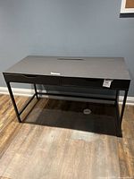 Front view of black desk with flat top and visible drawer cutouts on front.