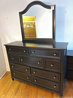 Front view of black wooden dresser with attached mirror showing nine drawers and arched mirror frame