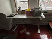 Front view of white electric standing desk under windows with various items on top