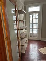 Full view of shelving unit in hallway space near door and radiator, showing five wooden shelves on white metal frame.