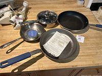 Overview of frying pans and small saucepan on wooden counter