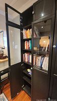 Image of two black Ikea bookcase panels with glass doors showing shelves with books and decorative items inside. Doors are open on one panel.