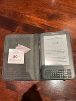Amazon Kindle D00901 ebook reader tablet inside a gray fabric cover, showing the keyboard and screen with 'Empty Battery' message.
