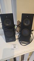 Two black Logitech computer speakers with wired connections, one speaker has control knobs and headphone jack.