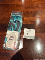 New Fitbit Flex wireless wristband inside unopened clear plastic packaging on wood surface with auction lot tag
