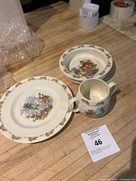 Photo showing three ceramic pieces: dinner plate, bowl, and cup arranged on wooden surface.