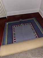 Photo showing the Pottery Barn area rug partially rolled at one end on a hardwood floor near a radiator and wall baseboard.